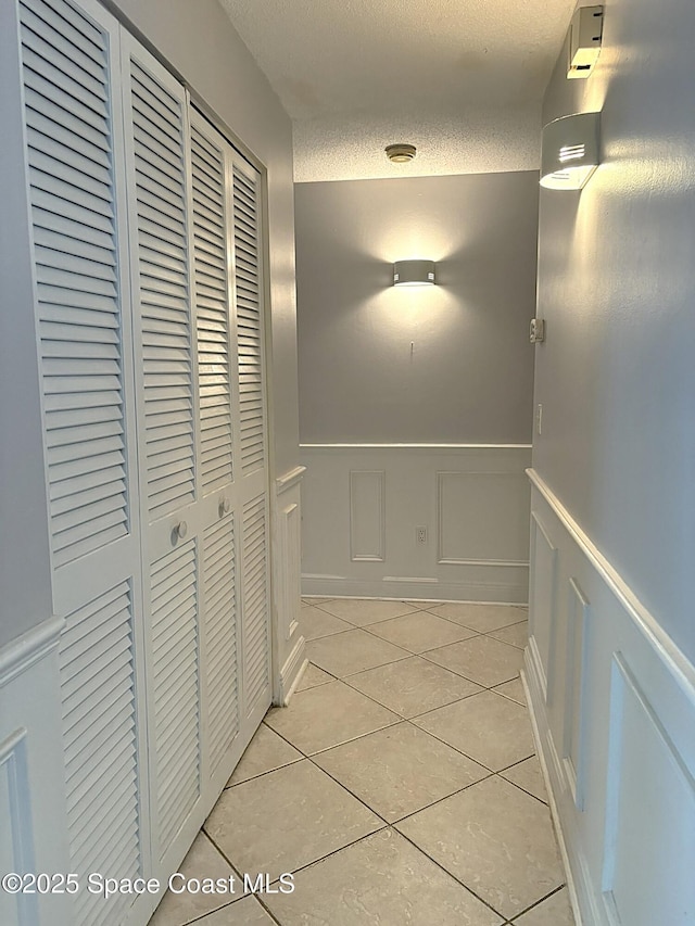 292 Pine Tree Dr, Indialantic, FL 32903 - hall featuring light tile patterned flooring, a wainscoted wall, a decorative wall, and a textured ceiling