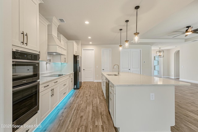 8025 Babcock St SE, Grant-Valkaria, FL 32909 - kitchen with stainless steel appliances, light wood-style flooring, white cabinetry, arched walkways, and an island with sink