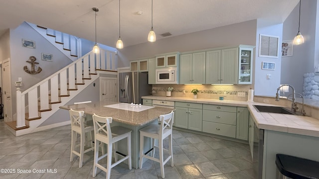 210 Pelican Dr, Melbourne Beach, FL 32951 - kitchen featuring stainless steel fridge with ice dispenser, white microwave, backsplash, green cabinetry, and a breakfast bar area