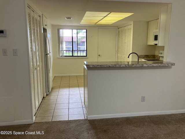 1515 Huntington Ln Unit 223, Rockledge, FL 32955 - kitchen with white appliances, a peninsula, white cabinetry, light tile patterned flooring, and light colored carpet