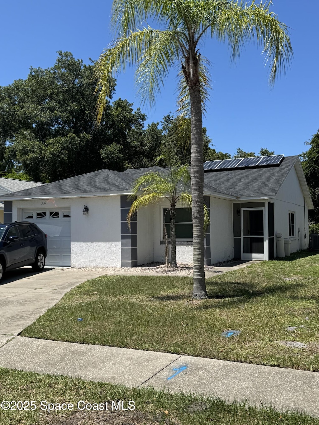 3116 Winchester Dr, Cocoa, FL 32926 - ranch-style home with an attached garage, roof mounted solar panels, a front lawn, driveway, and stucco siding