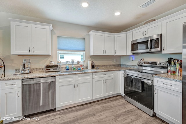 1689 Colorado St SE, Palm Bay, FL 32909 - kitchen featuring stainless steel appliances, white cabinetry, recessed lighting, light wood-type flooring, and light stone countertops