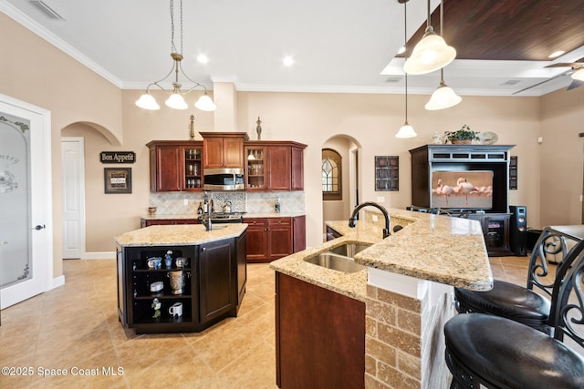 3079 Levanto Dr, Melbourne, FL 32940 - kitchen with arched walkways, stainless steel microwave, an island with sink, crown molding, and light tile patterned floors