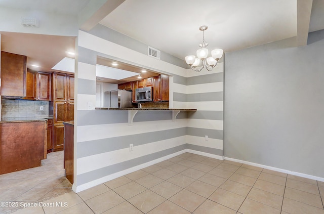 53 Emerald Ct, Satellite Beach, FL 32937 - kitchen featuring appliances with stainless steel finishes, light tile patterned floors, decorative backsplash, a chandelier, and brown cabinetry