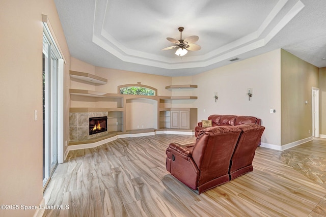 2604 Canary Isles Dr, Melbourne, FL 32901 - living room featuring a raised ceiling, ceiling fan, a tile fireplace, light wood-type flooring, and built in shelves