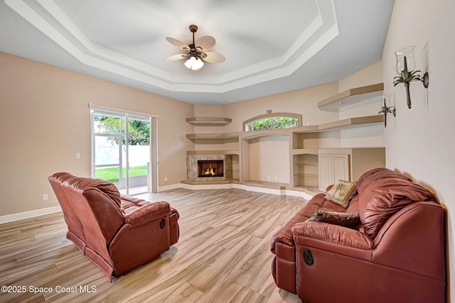 2604 Canary Isles Dr, Melbourne, FL 32901 - living room with a raised ceiling, light wood-style floors, a ceiling fan, and a warm lit fireplace