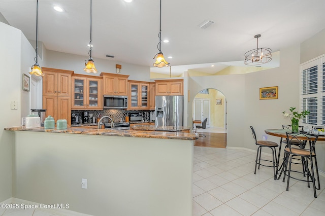 356 Fuller St SE, Palm Bay, FL 32909 - kitchen featuring stainless steel appliances, arched walkways, stone counters, a peninsula, and brown cabinetry