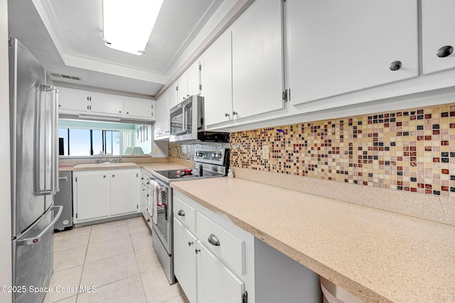 2467 S Washington Ave Unit 103B, Titusville, FL 32780 - kitchen with appliances with stainless steel finishes, light tile patterned floors, white cabinets, decorative backsplash, and light countertops