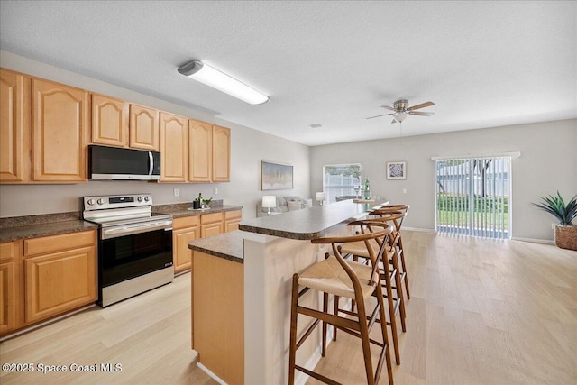 2605 Revolution St Unit 104, Melbourne, FL 32935 - kitchen with electric stove, a kitchen bar, light wood-style floors, light brown cabinets, and a textured ceiling