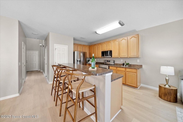 2605 Revolution St Unit 104, Melbourne, FL 32935 - kitchen with appliances with stainless steel finishes, light brown cabinets, light wood-style flooring, a kitchen bar, and a textured ceiling