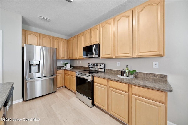 2605 Revolution St Unit 104, Melbourne, FL 32935 - kitchen with appliances with stainless steel finishes, light brown cabinets, dark countertops, light wood-style flooring, and a textured ceiling