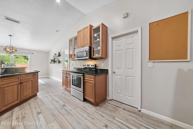 897 Hunters Creek Dr, Melbourne, FL 32904 - kitchen featuring stainless steel appliances, vaulted ceiling, dark countertops, light wood-style floors, and brown cabinetry