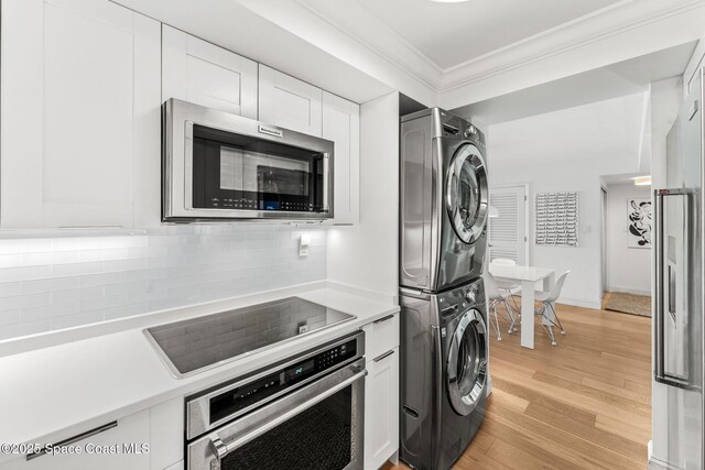 2100 N Atlantic Ave Unit 1110, Cocoa Beach, FL 32931 - kitchen with appliances with stainless steel finishes, stacked washer / dryer, ornamental molding, light countertops, and white cabinetry