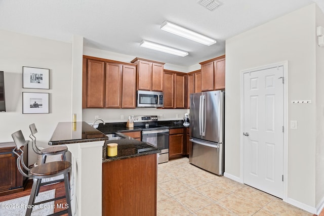 2710 Revolution St Unit 104, Melbourne, FL 32935 - kitchen featuring appliances with stainless steel finishes, a peninsula, a kitchen breakfast bar, light tile patterned floors, and brown cabinetry