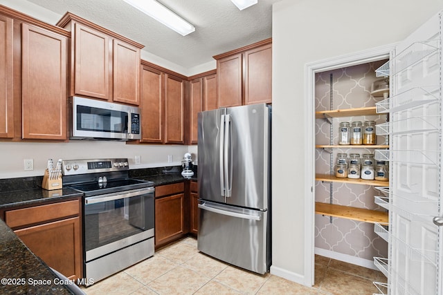 2710 Revolution St Unit 104, Melbourne, FL 32935 - kitchen featuring appliances with stainless steel finishes, light tile patterned flooring, dark stone counters, a textured ceiling, and brown cabinetry