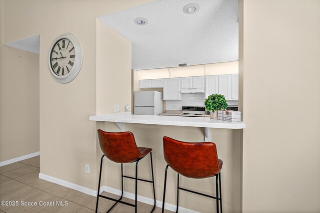 147 Ocean View Ln, Melbourne, FL 32903 - kitchen featuring white appliances, a kitchen bar, under cabinet range hood, light countertops, and a textured ceiling