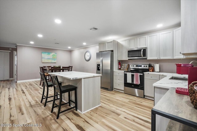 513 Ronnie Dr, Indian Harbour Beach, FL 32937 - kitchen featuring appliances with stainless steel finishes, a breakfast bar area, a kitchen island, light wood-type flooring, and crown molding