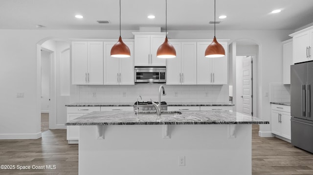 3110 Addison Dr, Melbourne, FL 32940 - kitchen featuring appliances with stainless steel finishes, arched walkways, wood finished floors, dark stone counters, and decorative backsplash