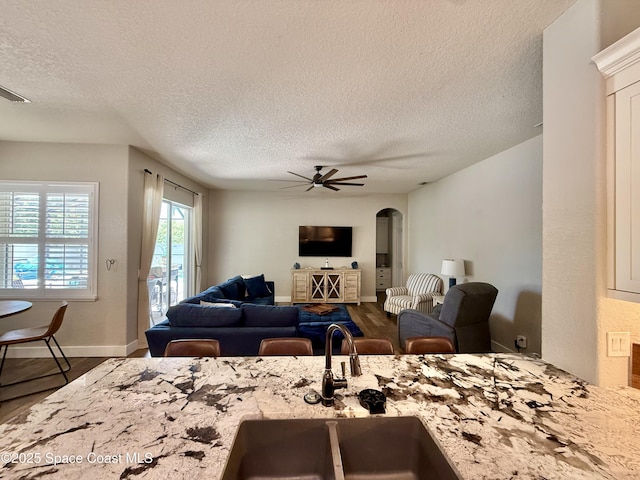 4569 Chastain Dr, Melbourne, FL 32940 - kitchen with a textured ceiling, arched walkways, light stone countertops, ceiling fan, and wood finished floors