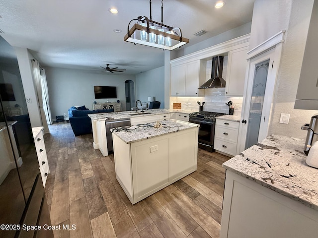 4569 Chastain Dr, Melbourne, FL 32940 - kitchen with black gas range, wall chimney exhaust hood, a peninsula, open floor plan, and a ceiling fan
