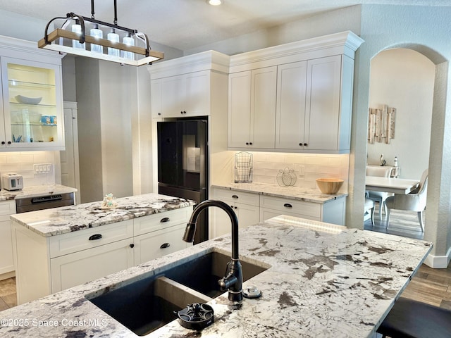 4569 Chastain Dr, Melbourne, FL 32940 - kitchen with black fridge, arched walkways, light wood-style flooring, decorative backsplash, and white cabinetry