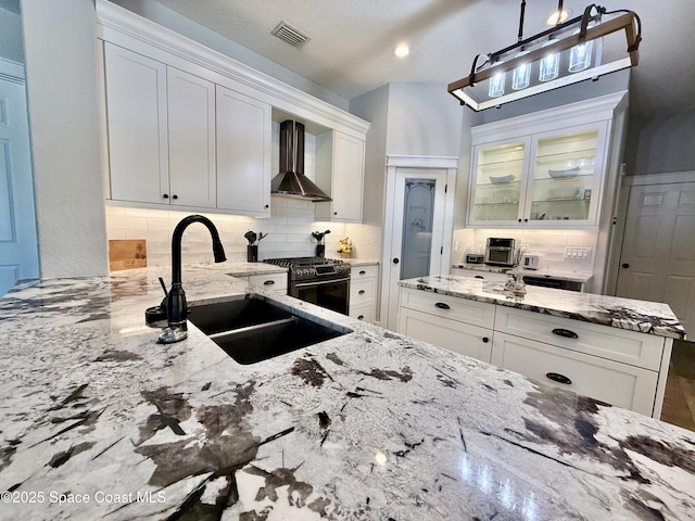 4569 Chastain Dr, Melbourne, FL 32940 - kitchen with wall chimney exhaust hood, stainless steel range with gas stovetop, tasteful backsplash, and white cabinetry