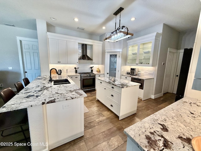 4569 Chastain Dr, Melbourne, FL 32940 - kitchen with stainless steel range with gas cooktop, wall chimney range hood, a peninsula, tasteful backsplash, and glass insert cabinets