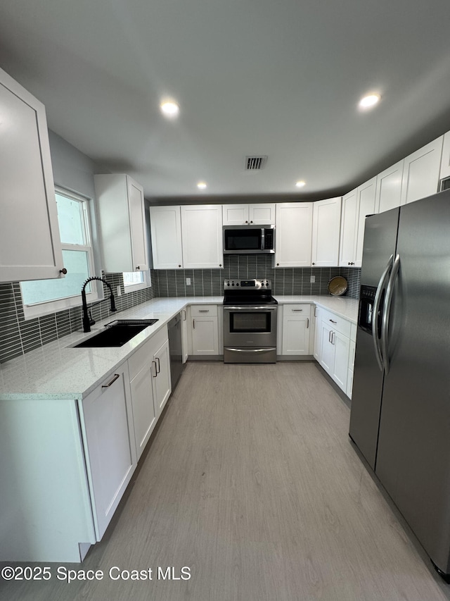 669 Vocelle Ave, Sebastian, FL 32958 - kitchen with stainless steel appliances, backsplash, light stone countertops, white cabinetry, and light wood-type flooring