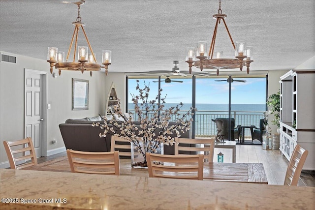 3221 S Atlantic Ave Unit 703, Cocoa Beach, FL 32931 - dining area with a chandelier, plenty of natural light, a textured ceiling, a ceiling fan, and a water view