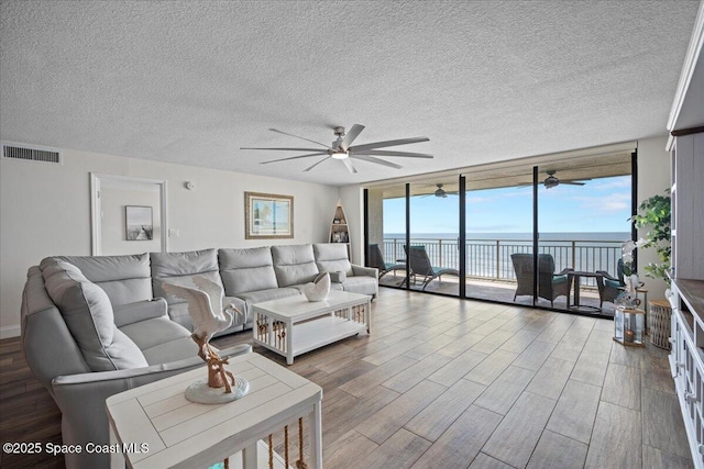 3221 S Atlantic Ave Unit 703, Cocoa Beach, FL 32931 - living area with ceiling fan, expansive windows, a water view, wood finished floors, and a textured ceiling