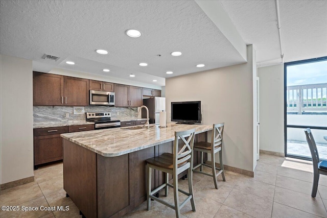 3221 S Atlantic Ave Unit 703, Cocoa Beach, FL 32931 - kitchen featuring stainless steel appliances, a textured ceiling, a breakfast bar area, decorative backsplash, and light tile patterned flooring