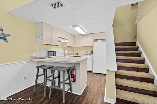8600 Ridgewood Ave Unit 1311, Cape Canaveral, FL 32920 - kitchen with white appliances, under cabinet range hood, dark wood-style floors, a peninsula, and wainscoting