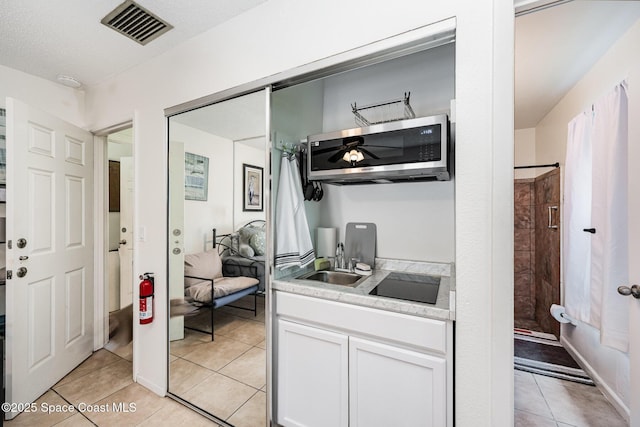 957 Stage St SE, Palm Bay, FL 32909 - kitchen with stainless steel microwave, light tile patterned floors, black electric stovetop, light countertops, and white cabinets