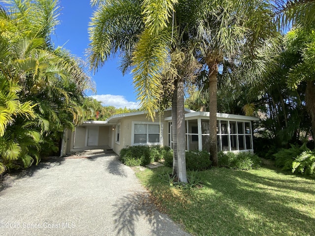 208 Johnson Ave, Cape Canaveral, FL 32920 - view of front facade with a sunroom, gravel driveway, a front lawn, and stucco siding