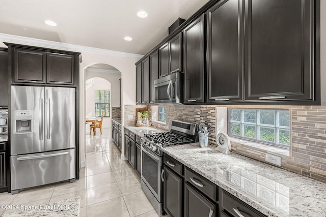 8522 Strom Park Dr, Melbourne, FL 32940 - kitchen featuring stainless steel appliances, arched walkways, light stone countertops, tasteful backsplash, and crown molding
