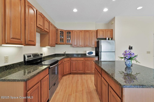 3825 Allen Ave, Micco, FL 32976 - kitchen with stainless steel appliances, light wood-style floors, glass insert cabinets, brown cabinetry, and dark stone counters