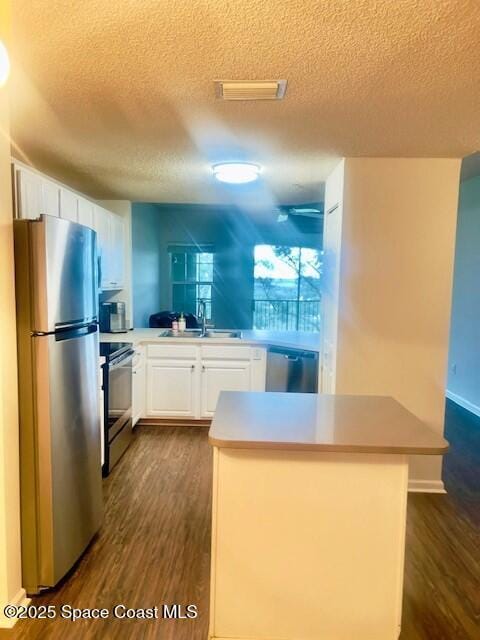 1070 Bella Vista Blvd Unit 110, Saint Augustine, FL 32084 - kitchen featuring appliances with stainless steel finishes, a textured ceiling, dark wood finished floors, white cabinetry, and a center island