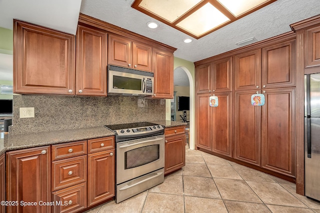 63 Yacht Haven Dr, Cocoa Beach, FL 32931 - kitchen featuring stainless steel appliances, arched walkways, tasteful backsplash, light tile patterned floors, and brown cabinets