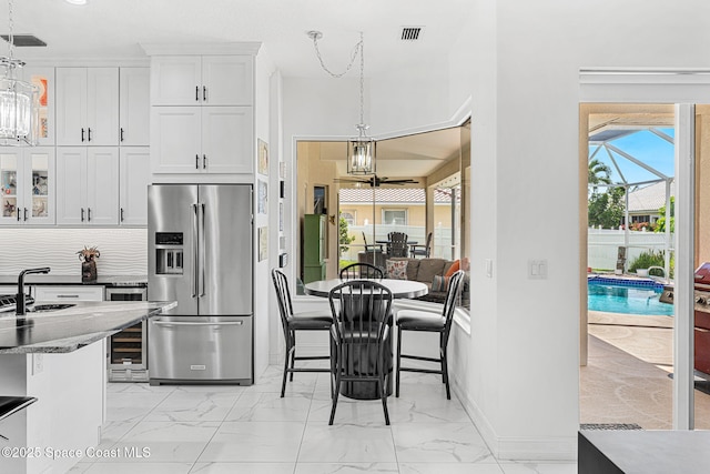227 Loggerhead Dr, Melbourne Beach, FL 32951 - kitchen featuring a chandelier, high end fridge, light marble finish flooring, wine cooler, and white cabinetry