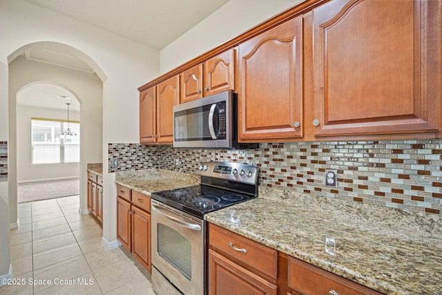 2690 Cypress Tree Trl, Saint Cloud, FL 34772 - kitchen featuring appliances with stainless steel finishes, light tile patterned floors, light stone counters, tasteful backsplash, and arched walkways