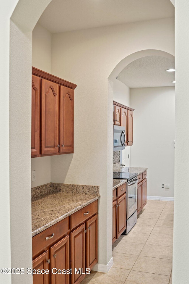 2690 Cypress Tree Trl, Saint Cloud, FL 34772 - kitchen featuring stainless steel appliances, arched walkways, light tile patterned flooring, light stone countertops, and brown cabinetry