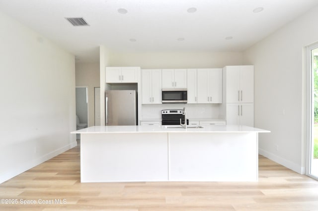 1043 Walden Blvd SE, Palm Bay, FL 32909 - kitchen featuring appliances with stainless steel finishes, white cabinets, a kitchen island with sink, light countertops, and light wood-type flooring