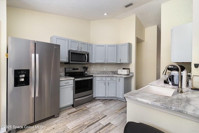 2606 Tepee Ave SE, Palm Bay, FL 32909 - kitchen with appliances with stainless steel finishes, vaulted ceiling, decorative backsplash, light wood-style flooring, and light stone counters