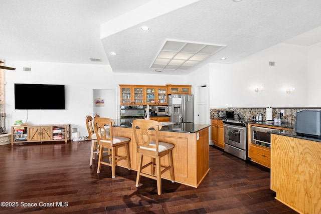 405 Lake View Ln, Grant-Valkaria, FL 32909 - kitchen with appliances with stainless steel finishes, dark countertops, a kitchen bar, glass insert cabinets, and dark wood-style flooring