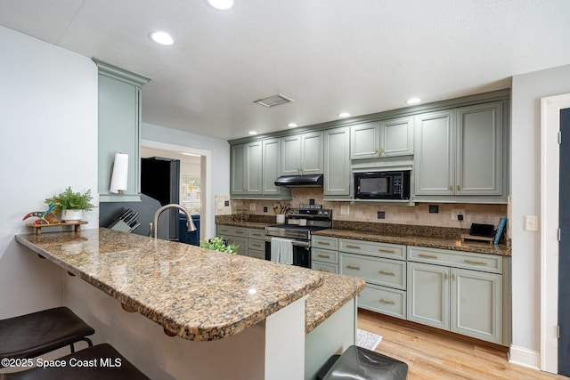 560 Conifer St, Melbourne, FL 32904 - kitchen with stainless steel electric range oven, black microwave, a kitchen breakfast bar, light wood finished floors, and a peninsula