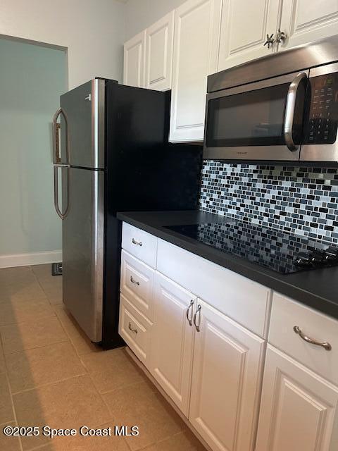 351 Taylor Ave Unit E5, Cape Canaveral, FL 32920 - kitchen with stainless steel microwave, light tile patterned floors, backsplash, dark countertops, and white cabinets