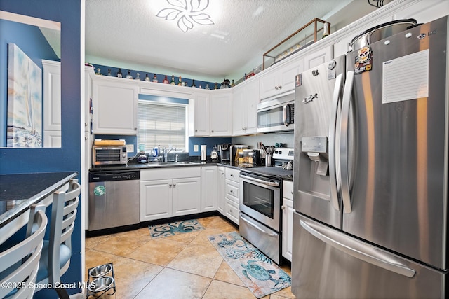 113 Surf Dr, Cocoa Beach, FL 32931 - kitchen featuring appliances with stainless steel finishes, white cabinets, a textured ceiling, light tile patterned floors, and dark stone countertops