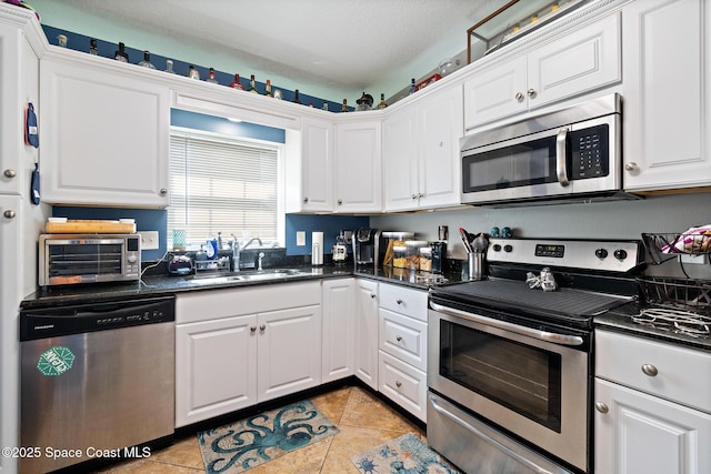 113 Surf Dr, Cocoa Beach, FL 32931 - kitchen with stainless steel appliances, dark countertops, white cabinetry, and light tile patterned floors