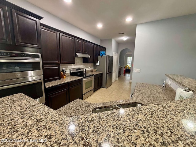 3725 Aria Dr, Melbourne, FL 32904 - kitchen featuring stainless steel appliances, arched walkways, decorative backsplash, light stone countertops, and recessed lighting