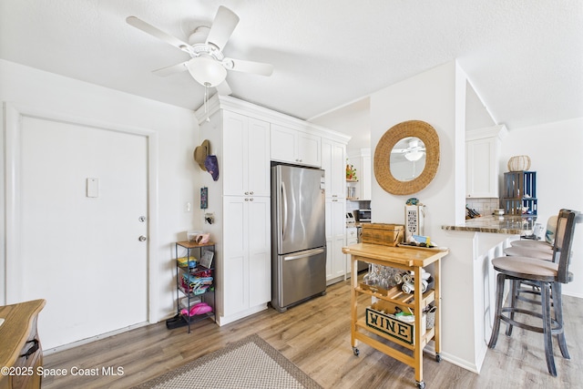 3190 N Atlantic Ave Unit 220, Cocoa Beach, FL 32931 - kitchen with freestanding refrigerator, light wood-style floors, a ceiling fan, and a kitchen breakfast bar